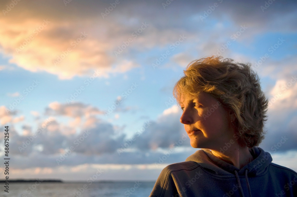 Woman with sunset light illuminating her face, at Leech Lake in Minnesota, USA; Walker, Minnesota, United States of America Woman with sunset light illuminating her face, at Leech Lake in Minnesota, USA; Walker, Minnesota, United States of America