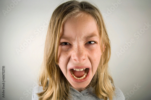 Preteen girl with an angry expression against a grey background; Studio photo