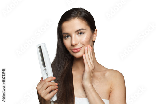 Healthy young adult woman using hair iron and straightening her long brown hair on white background, studio fashion beauty portrait. Hair ironing and hairstyle concept