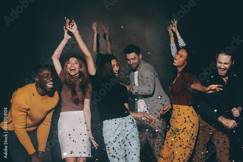 Group of young people dancing and having fun in night club together while confetti flying around