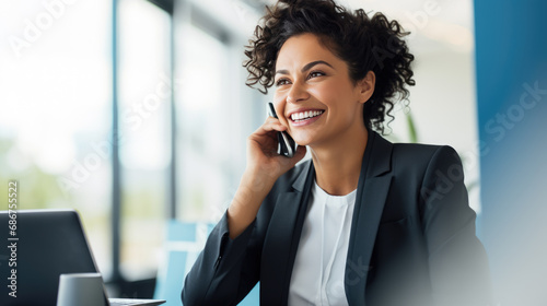 Cheerful woman in an office setting, talking on the phone with a laptop in front of her photo