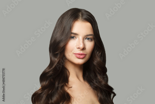 Beautiful brunette model woman with long wavy hair and shiny fresh skin posing on white background, fashion beauty studio portrait