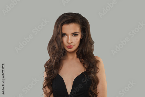 Perfect fashion model with dark healthy hairstyle, fresh clean skin and trendy make-up looking at camera on gray background. Brunette woman portrait