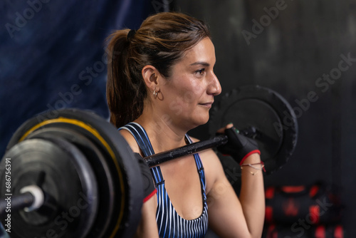 Mexican latina adult female holding a barbell at face level in a gymnasium