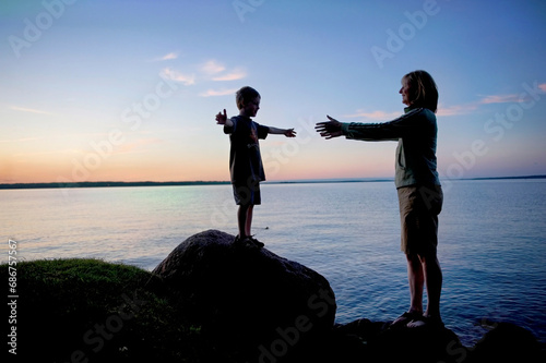 Mother helps her young son off a boulder along Leech Lake at sunset; Walker, Minnesota, United States of America photo