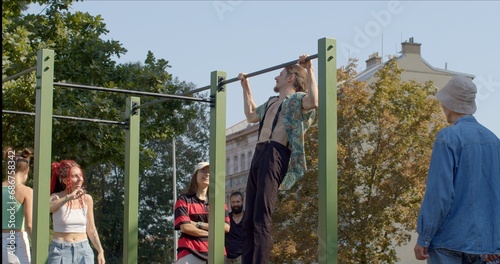 Young man performs impressive tricks on horizontal bar in an urban workout area. Showcases a sporty, healthy physique, reflecting dedication to physical fitness. 10.09.23 Folimanka, Prague, CZ photo