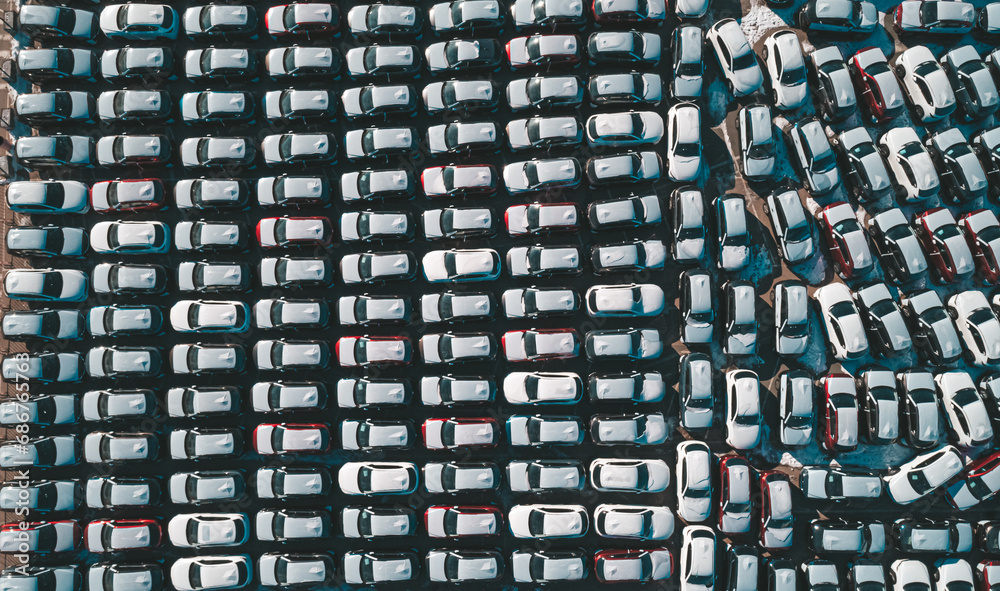 Fototapeta premium Aerial top down view of new cars parked in car parking lot. Car dealer parking lot full of new automobiles. New cars lined up for import and export business.