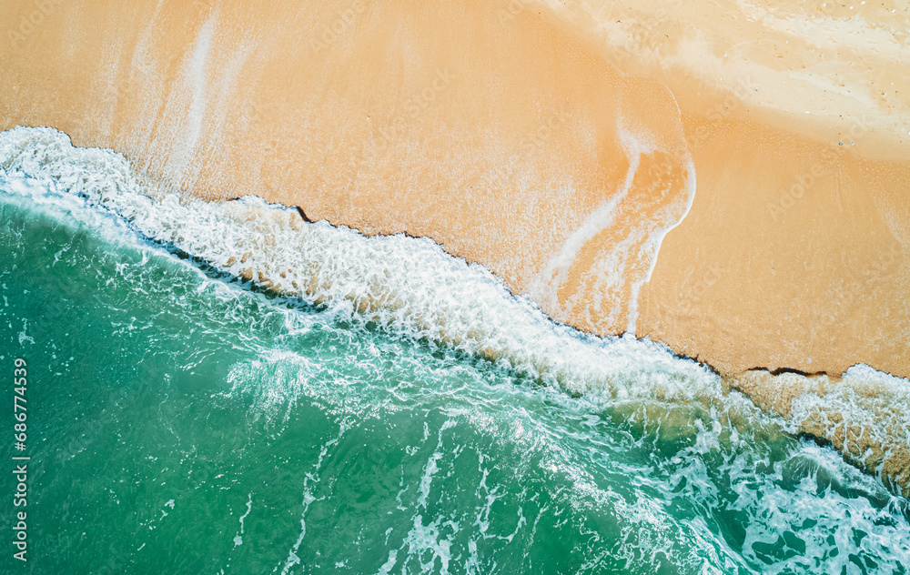 Aerial view of sandy beach and turquoise ocean. Top view of ocean waves reaching shore on sunny day.