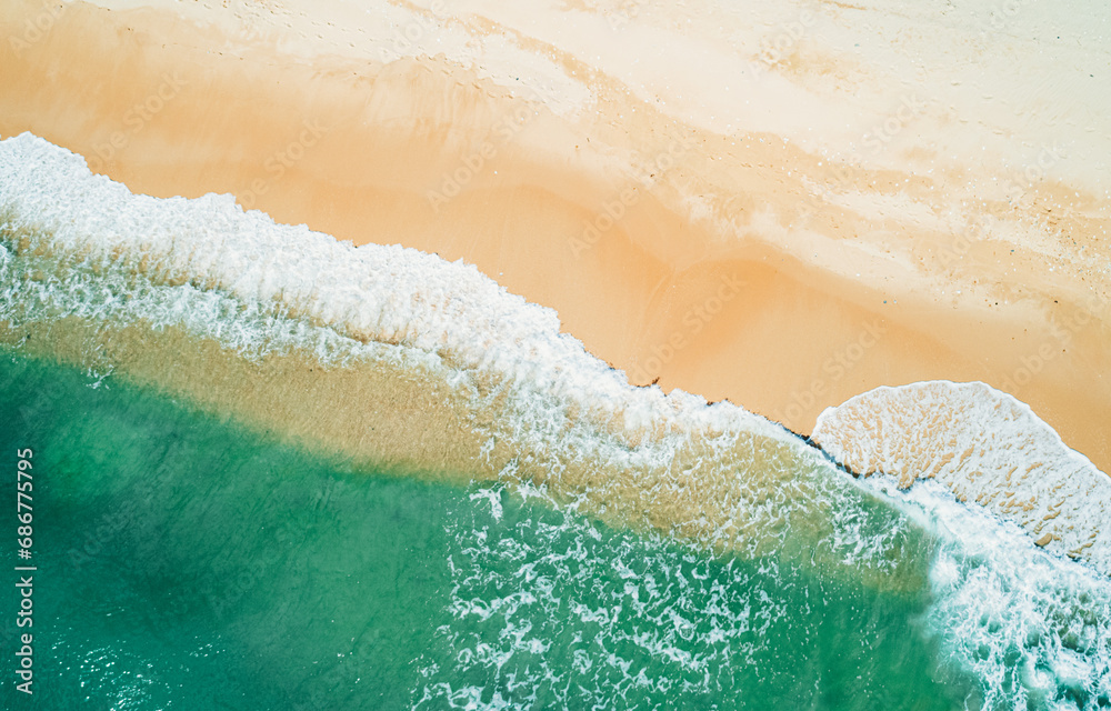 Aerial view of sandy beach and turquoise ocean. Top view of ocean waves reaching shore on sunny day.