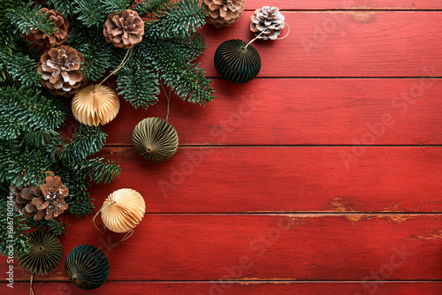 Christmas composition. Christmas fir tree branches with pine cones and papers rustic balls on wooden red rustic background. Christmas greeting card. Flat lay, top view. Copy space. Banner backdrop.