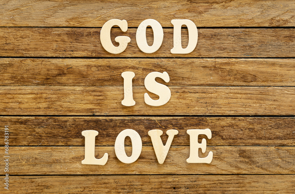 The inscription God is love made of wooden letters on a wooden background, top view.