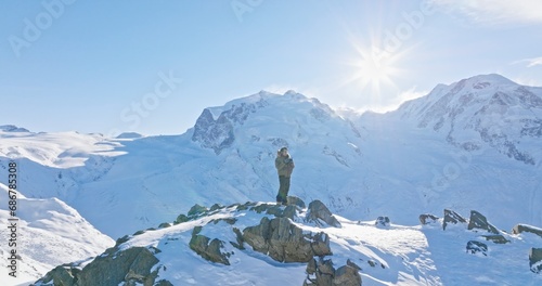 Panoramic landscape of Young asian man standing on top of the famous Gornergrat observatory operates with drone remote control with iconic famous Matterhorn sunset background. Swiss alps, Switzerland.