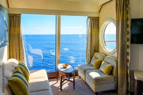 A bowl of fruit sits on a table in a luxury cruise ship cabin with a large window and porthole to balcony as it sails on a blue Mediterranean Sea. photo