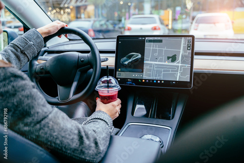 Rear view of unrecognizable female driving modern electric car. Tesla tablet screen.