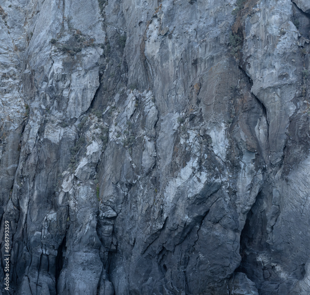 Weathered seaside rock face texture. Aged volcanic stone wall surface background pattern with cracks and scratches. Ischia Island, Italy.