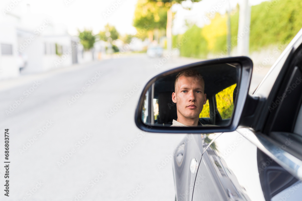 Reflection of young man in wing mirror of a car