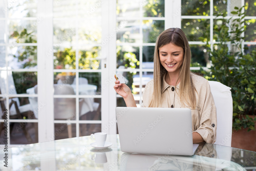 Happy young woman holding credit card while using laptop at table in coffee shop Happy young woman holding credit card while using laptop at table in coffee shop