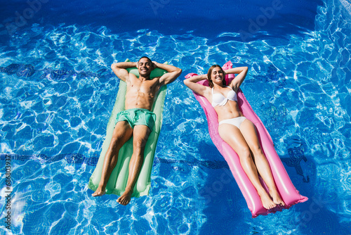 Smiling young couple with hands behind head relaxing on airbeds in swimming pool photo