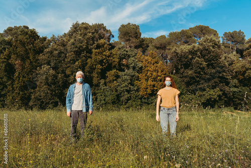 Woman and senior man with masks standing on meadow, safety distance