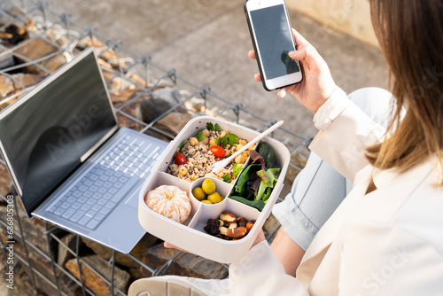 Female entrepreneur using smart phone while holding reusable lunch box