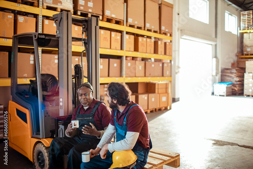 Two Warehouse Workers on Break with Coffee and Forklift in Background photo