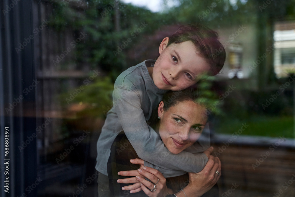 Loving son embracing mother while standing at home seen through window