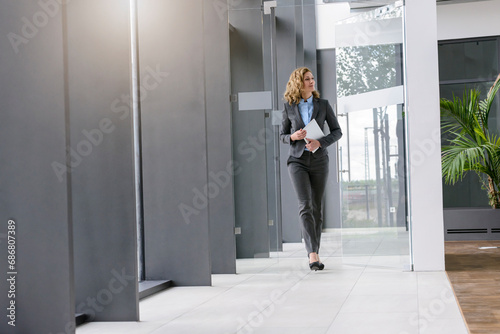 Confident businesswoman holding tablet walking in office