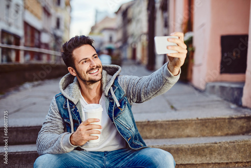 Man taking selfie holding coffee and sitting on stairs photo