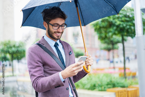 Fashionable businessman with umbrella checking his cell phone in the city © tunedin