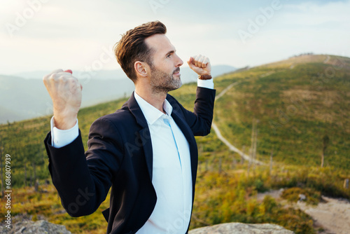 Self-confident businessman standing on top of a mountain photo