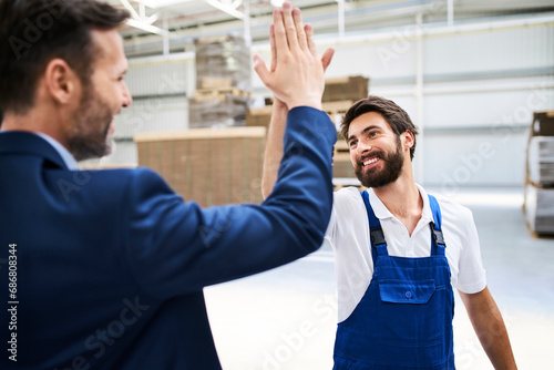 Happy businessman and worker high fiving in a factory photo