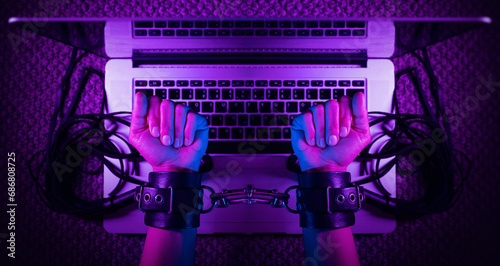 female sexy hands in bdsm handcuffs with laptop in neon light on dark background