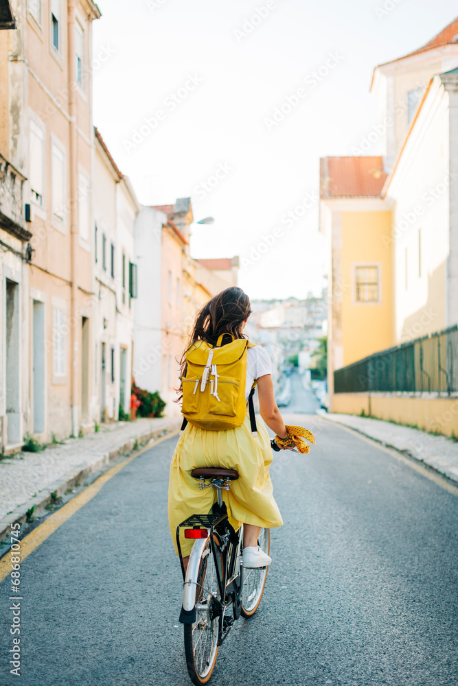 Woman with backpack riding bicycle on road amidst buildings in city