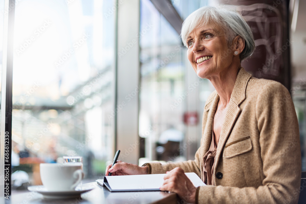 Smiling senior businesswoman taking notes in a cafe Smiling senior businesswoman taking notes in a cafe