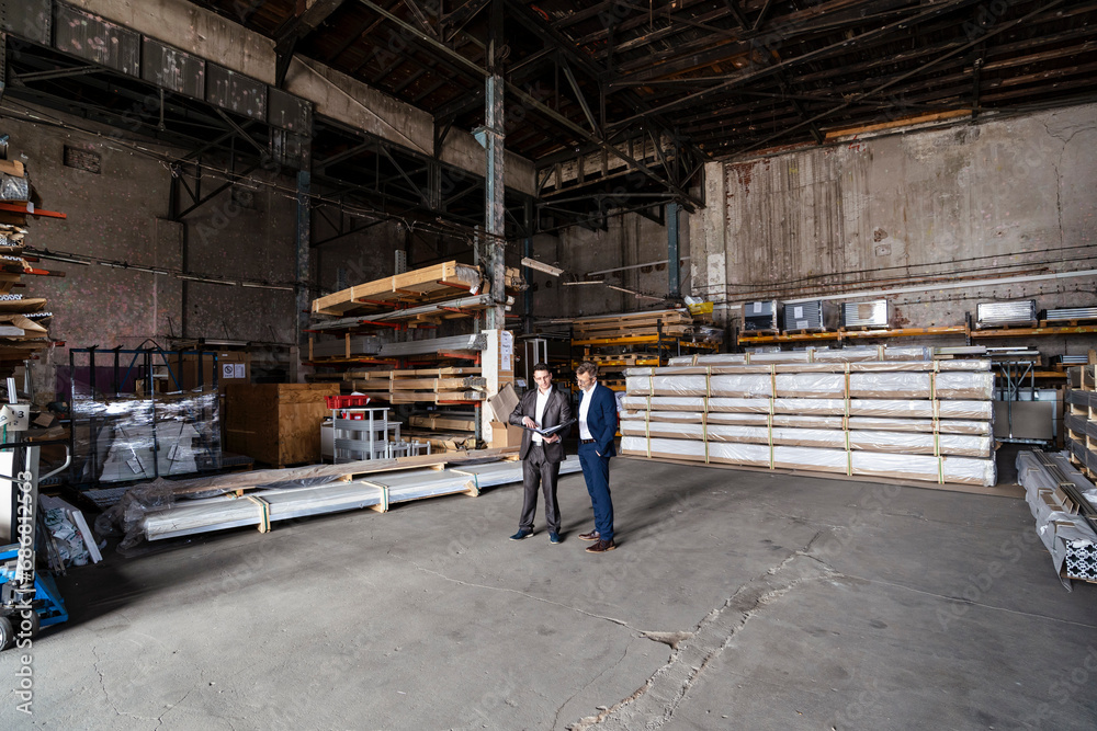 Two businessmen with folder talking in an old storehouse Two businessmen with folder talking in an old storehouse
