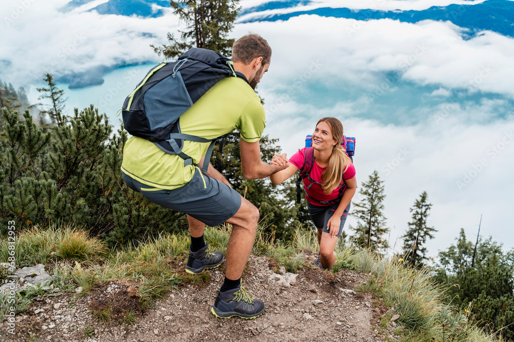 Young man helping girlfriend on a hiking trip in the mountains, Herzogstand, Bavaria, Germany