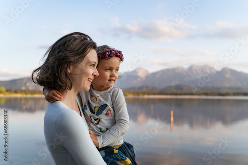 Smiling mother carrying cute daughter while standing against lake at sunset © tunedin