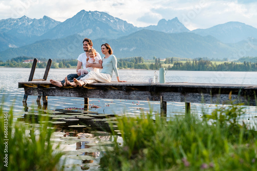 Happy family looking at view while sitting on jetty over lake against mountains © tunedin