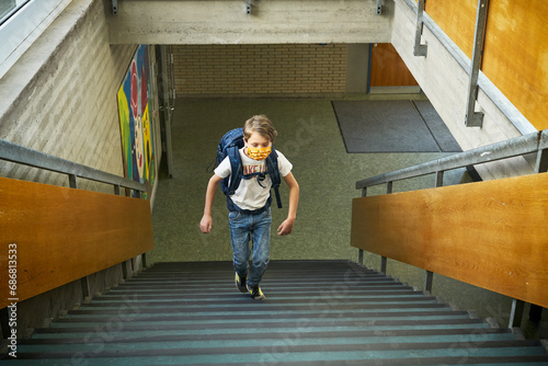 Boy wearing mask in school walking up stairs photo