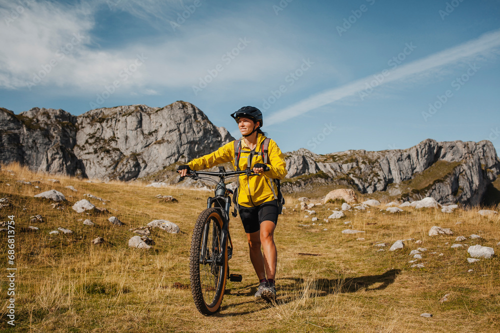 Fototapeta premium Mid adult woman holding bicycle while against mountain at Somiedo Natural Park, Spain