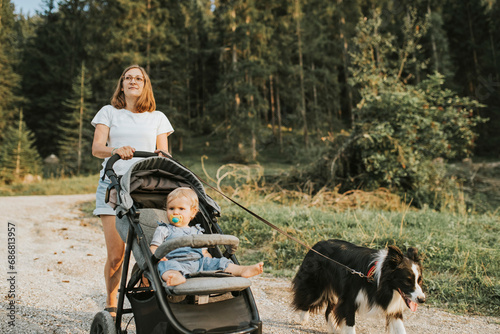 Mother with baby in stroller and dog walking on forest path © tunedin