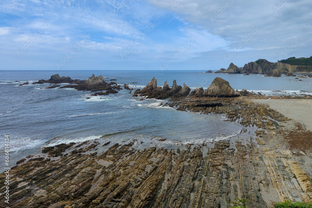 a rocky beach with jagged rocks and cliffs in the background, taken on a day with a light blue sky