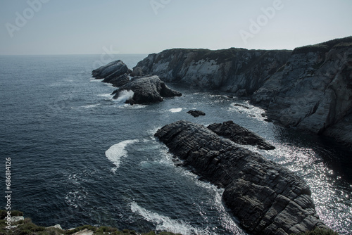 a rocky coastline with the ocean and cliffs in the background, taken from a high vantage point on a sunny day photo