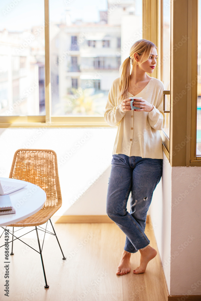 Blonde woman with cup of coffee looking out of the window Blonde woman with cup of coffee looking out of the window
