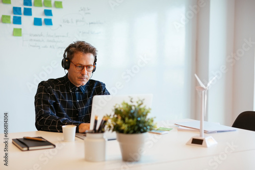 Businessman wearing headphones using laptop at desk in office photo