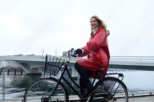Denmark, Copenhagen, happy woman riding bicycle at the waterfront in rainy weather