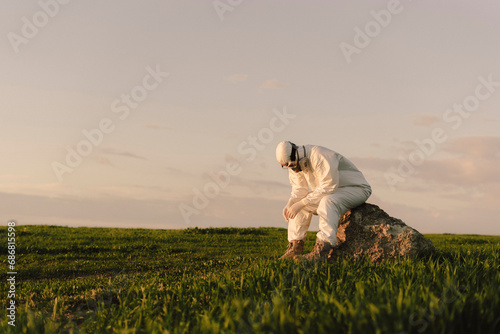 Man wearing protective suit and mask sitting on a rock in the countryside