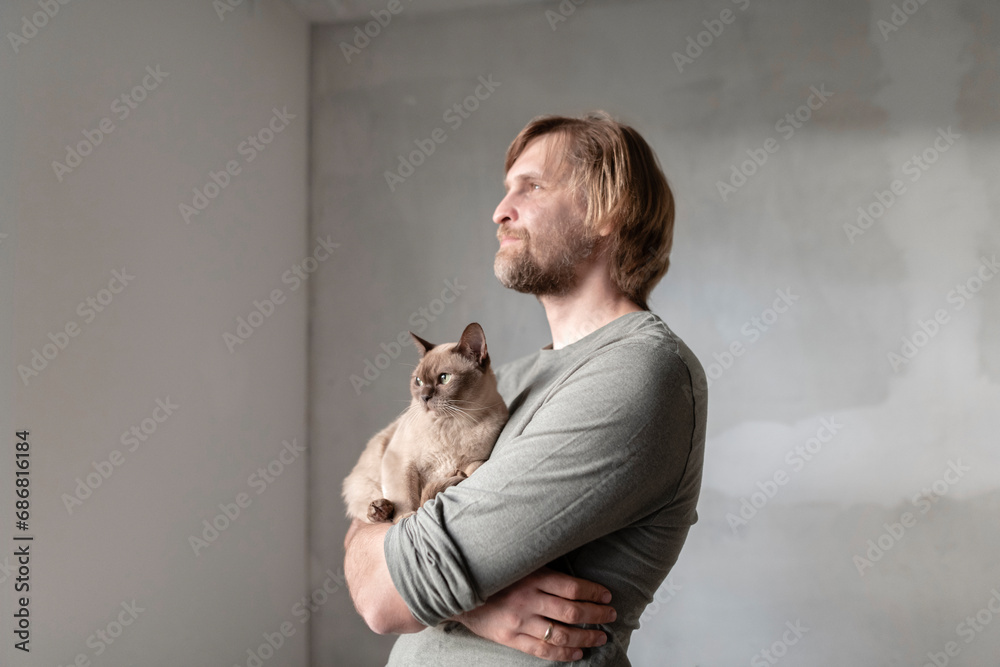 Thoughtful man carrying Burmese cat during home renovation