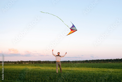 Mid adult man flying kite while standing on grassy landscape against sky at sunset