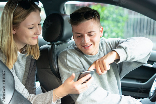 Smiling young couple in a car looking at cell phone
